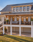 Rear exterior view of Islabella, showing the covered rear porch on the main floor, the stair down to the yard, the second-floor dormer with a row of five windows and the two garage doors on the side.