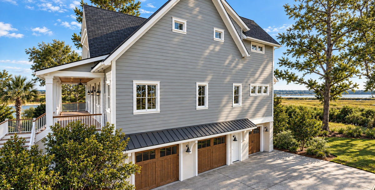 Garage side view of The Curtis in daylight, showing the long gray wall, the side porch, and wood garage doors under a metal shed roof at ground level, including the smaller golf cart bay