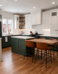 Kitchen in a built Tilbury Lane, with the 18-foot eat-in island seating four, green base cabinets, white uppers and the open stair beyond.